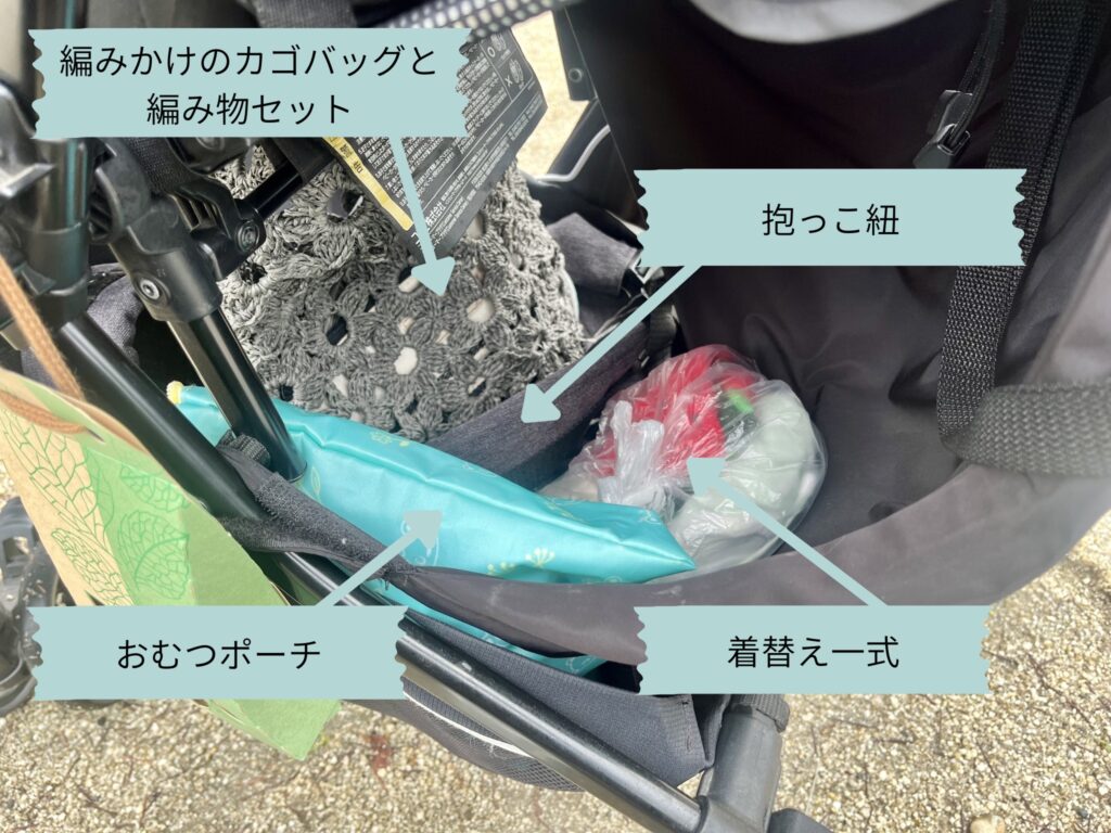 ベビーカーの下段荷物入れに収納された、編みかけのカゴバッグ、おむつポーチ、抱っこ紐、お着替え一式